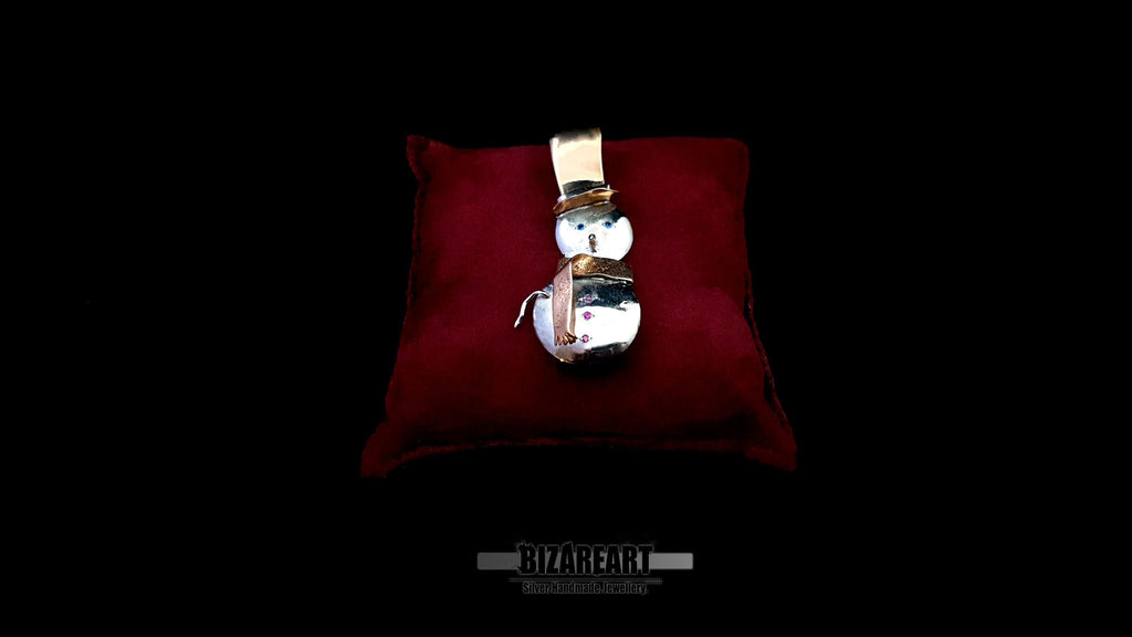 Detailed close-up of the snowman pendant on a red velvet cushion, highlighting the high-shine 925 silver body and rose gold plated scarf.