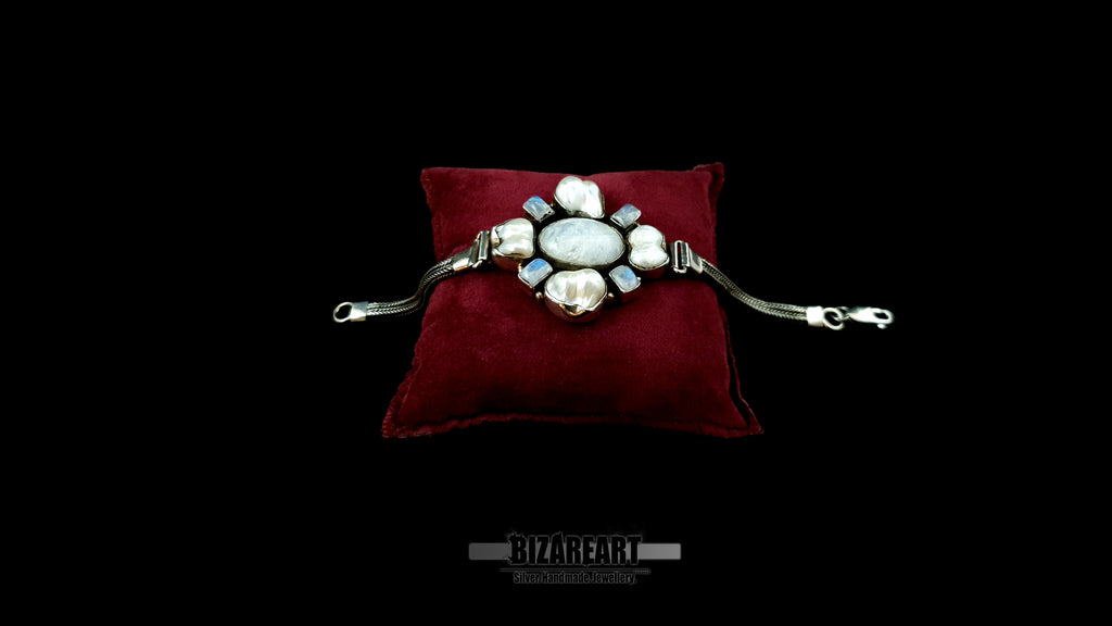Angled view of artisan silver bracelet featuring dual-strand woven chains and a central diamond-shaped cluster of iridescent labradorite and pearls on a velvet mount.