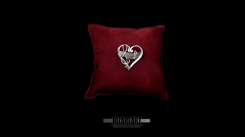 Hand-forged sterling silver heart melody pendant resting on a luxurious deep red velvet pillow, centered against a dramatic black background with a clean brand watermark below.